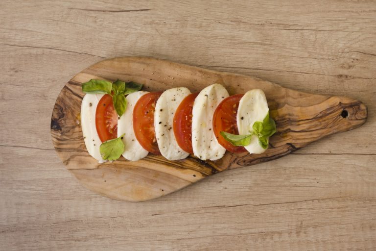 slices-mozzarella-cheese-tomatoes-with-herb-chopping-board-against-wooden-backdrop